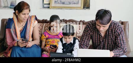 Indian family using various technologies while sitting on sofa at home Stock Photo