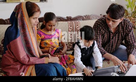 Indian family using various technologies while sitting on the sofa at home Stock Photo