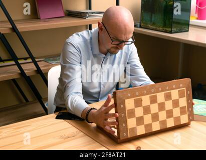 Young bald bearded thoughtful man open box with chess pieces on table. In finding solution, on. Thinking about strategy Stock Photo
