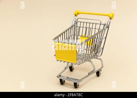 Metal shopping cart on a beige background. Concept objects for supermarket. Photo with place for your text and design. Stock Photo