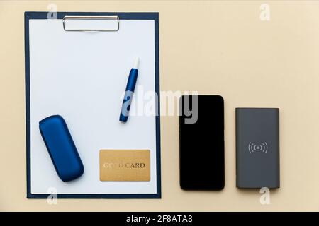 Electronic blue iQos cigarette, telephone, power bank and folder with clip  paper a4 on beige background. Photo with place for your text, logo and desi  Stock Photo