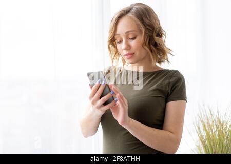 Pregnant woman use smartphone standing near big window Pregnancy Caucasian female with cell phone Modern technology concept Stock Photo