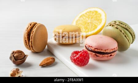Variety of french macaroons with raspberry, nuts and lemon on white wooden table. French meringue cookie macarons. Stock Photo