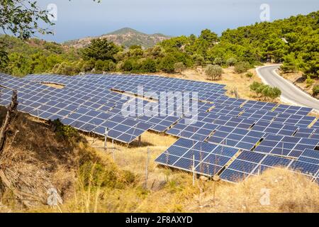 Beautiful modern solar station with blue panels standing in field with green grass and mountains at the horizon under a bright cloudy sky with reflect Stock Photo