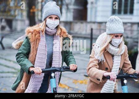 Girl friends wearing face masks and commuting on scooter in the city Stock Photo