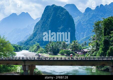 Laotians elementary schoolchildren walking past concrete bridge over the Nam Song River at dusk. Magical mountains range in the Background. Laos. Stock Photo