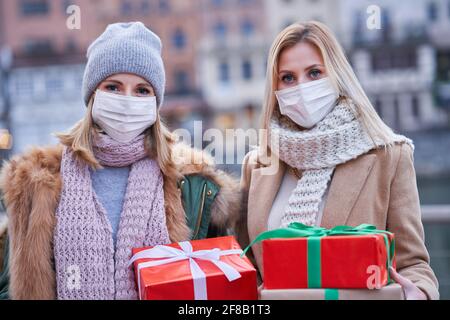 Two women wearing masks and holding Christmas presents in the city Stock Photo