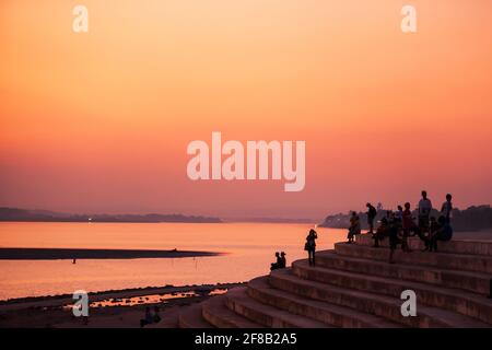 Tourists and Laotians relaxing on the Mekong River terrace view at sunset. Dramatic sunset sky in the background. Vientiane, Laos. Stock Photo