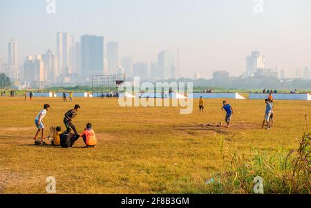 MUMBAI, INDIA - December 29, 2021: Kids playing cricket in a park in Mumbai with skyscrapers in the background Stock Photo