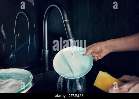 Male hand close-up washing a blue plate on dark background. Stock Photo