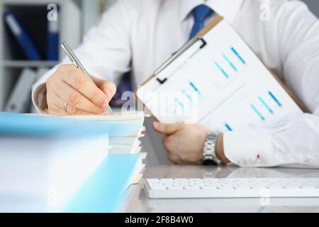 Businessman holds clipboard with commercial charts in his hands and makes notes in documents Stock Photo