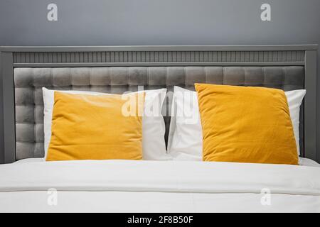 Bed with gray color velvet headboard and bright yellow pillows. Stock Photo
