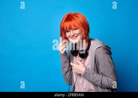 hipster girl with headphones on blue background. smiling teenager with red hair Stock Photo