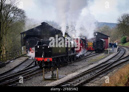 Historic steam trains or locos puffing clouds of smoke (engine driver in cab & enthusiasts watching) - Oxenhope Station sidings, Yorkshire, England UK Stock Photo