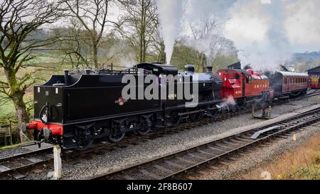 Historic steam trains or locos puffing clouds of smoke on heritage railway (engine driver in cab) - Oxenhope Station sidings, Yorkshire, England UK. Stock Photo