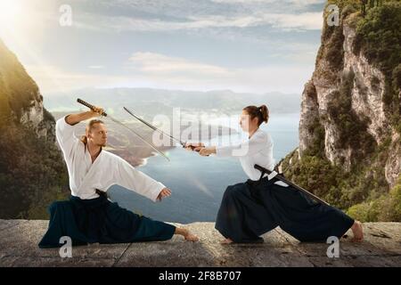 Man and woman, teacher fighting Aikido, training martial arts on meadow in front of lake and mountains Stock Photo