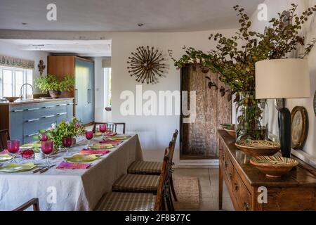 Table for eight with walls in 'Clean White' and view to kitchen in modernised Grade II listed Suffolk farmhouse. Stock Photo
