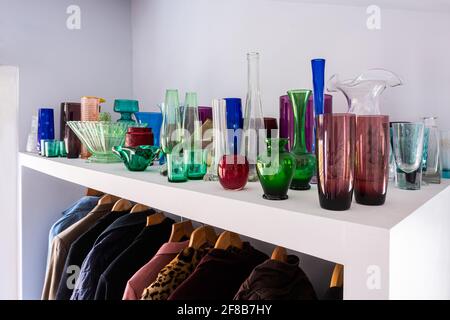 Collection of glass on shelf above coats, a jewel-like display. Stock Photo