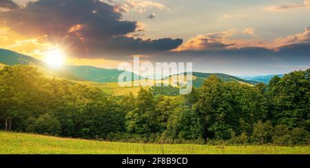 summer landscape of carpathian mountains at sunset. beautiful scenery in evening light. beech forest and grassy alpine meadows on the hills. clouds on Stock Photo