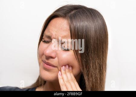 Young woman touching her cheek because of strong tooth pain. Female suffering from toothache. Woman face with painful expression. Teeth problem Stock Photo