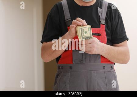 Builder in overalls and protective mask, transferring his salary for work performed on the construction site. Close-up view focused on money Stock Photo