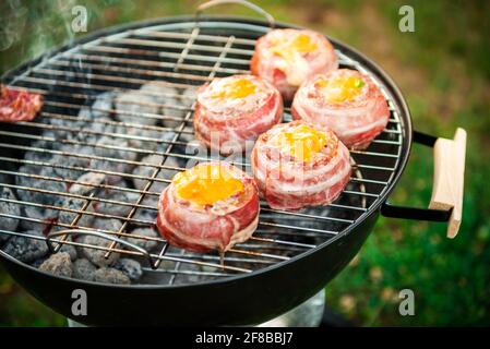 Making home made Beer Can Bacon Burgers on barbecue grill. Preparing stuffed patties, wrapped  in bacon and grilling on indirect heat in nature at bac Stock Photo