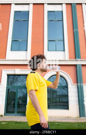 young latin male athlete wearing yellow t-shirt drinks water after a training session Stock Photo