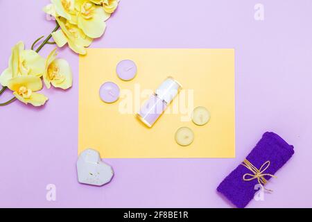 Scented candles, towel,  lotion and orchid flowers on a yellow and purple background. Top view, copy space. Spa concept, flat lay. Stock Photo