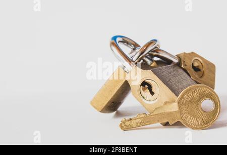 Closeup of a brass key in front of three interlinked padlocks on a white background Stock Photo