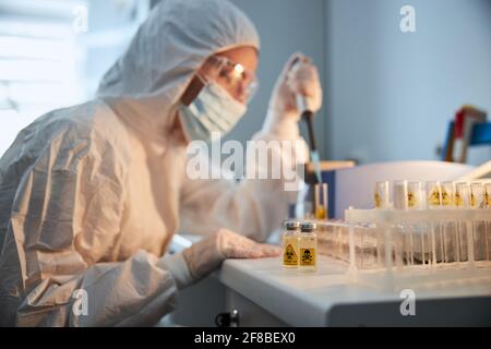 Experienced researcher in a hazmat suit working on a COVID vaccine Stock Photo