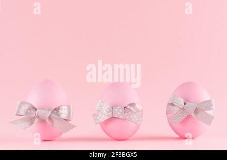 Pink easter eggs with grey bows standing in row on pastel pink background. Stock Photo