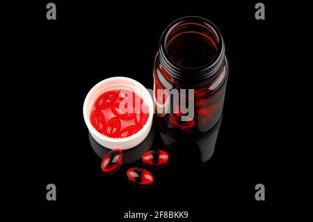Red vitamin pills in vial on glossy black background Stock Photo