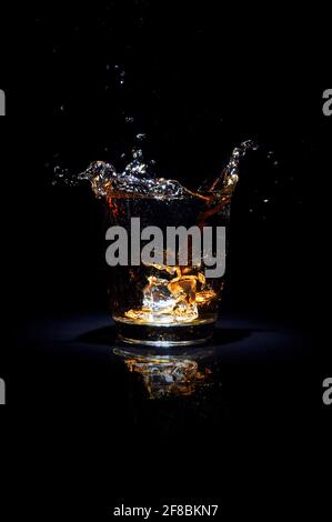 Glass of whiskey with splash, on black background Stock Photo