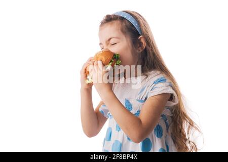 Little girl eating big burger. Kid looking at healthy big sandwich, studio isolated on white background. Stock Photo