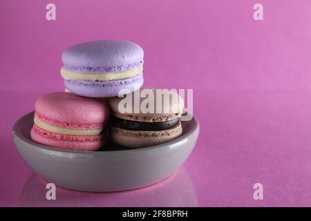 Macaroons three multicolored on a gray saucer plate stands on a pink background with a place for text and copyspace. Stock Photo