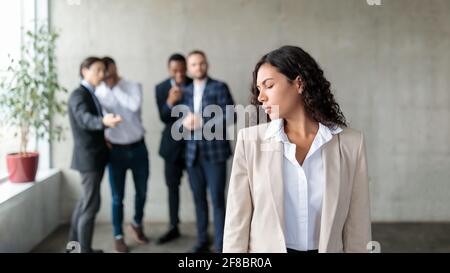 Group Of Businessmen Whispering Behind Back Of Businesswoman In Office Stock Photo