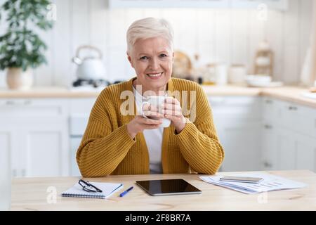 Happy elderly woman having coffee break while studying online Stock Photo