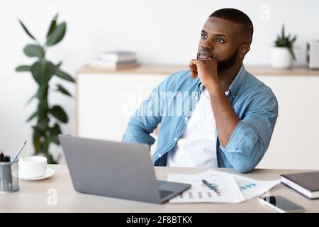 Black Freelancer Guy Sitting At Workplace With Thoughtful Face Expression Stock Photo