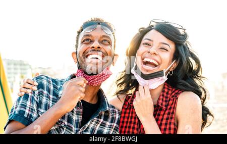 Young couple in love laughing over open face mask - New normal life style and relationship concept with happy lovers on positive mood at beach Stock Photo