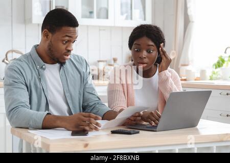 Portraif Of Shocked Black Spouses Checking Financial Documents In Kitchen Stock Photo