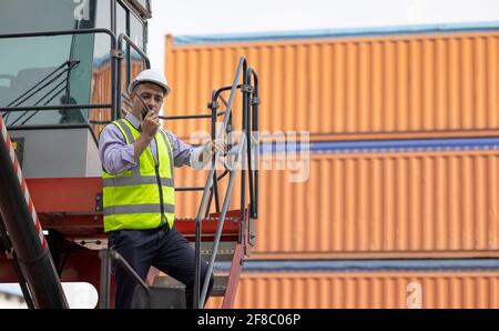 Man engineer using walkie-talkie in shipping yard, Industrial worker is controlling container loading by walkie talkie in import-export business. Stock Photo