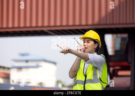 woman factory worker or engineer using walkie talkie and calling someone for preparing a job in containers warehouse storage Stock Photo