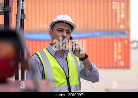 Worker helmet standing and talking on mobile phone at logistic cargo containers shipping yard Stock Photo