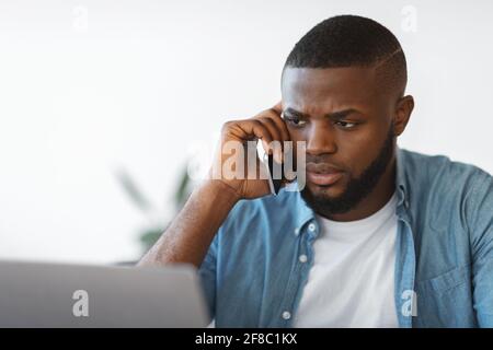 Portrait Of Busy African Man Talking On Cellphone And Working On Laptop Stock Photo