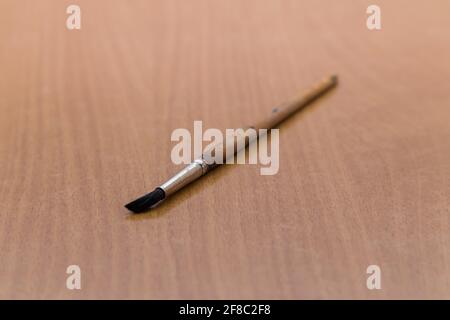 An artistic brush with a wooden handle lies on the table, one close-up. A tool for painting with paints on the artist's desk. There is copy space. Warm soft daylight. Stock Photo