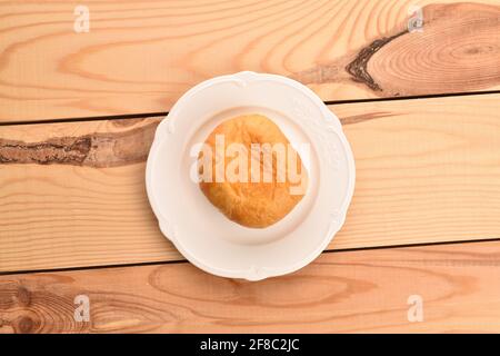 One freshly baked appetizing, tasty, sweet donut with cherry filling on a white ceramic saucer, close-up, on a background of a table made of wood Stock Photo