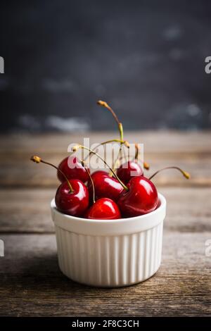 Ripe and juicy cherries in white ceramic bowl on the dark rustic background. Selective focus. Shallow depth of field. Stock Photo