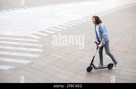 Excited guy having pleasant ride on electric kick scooter Stock Photo