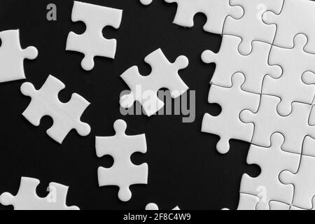 Unfinished white jigsaw puzzle pieces on black background Stock Photo