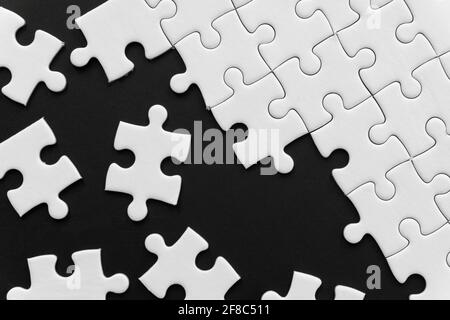 Unfinished white jigsaw puzzle pieces on black background Stock Photo